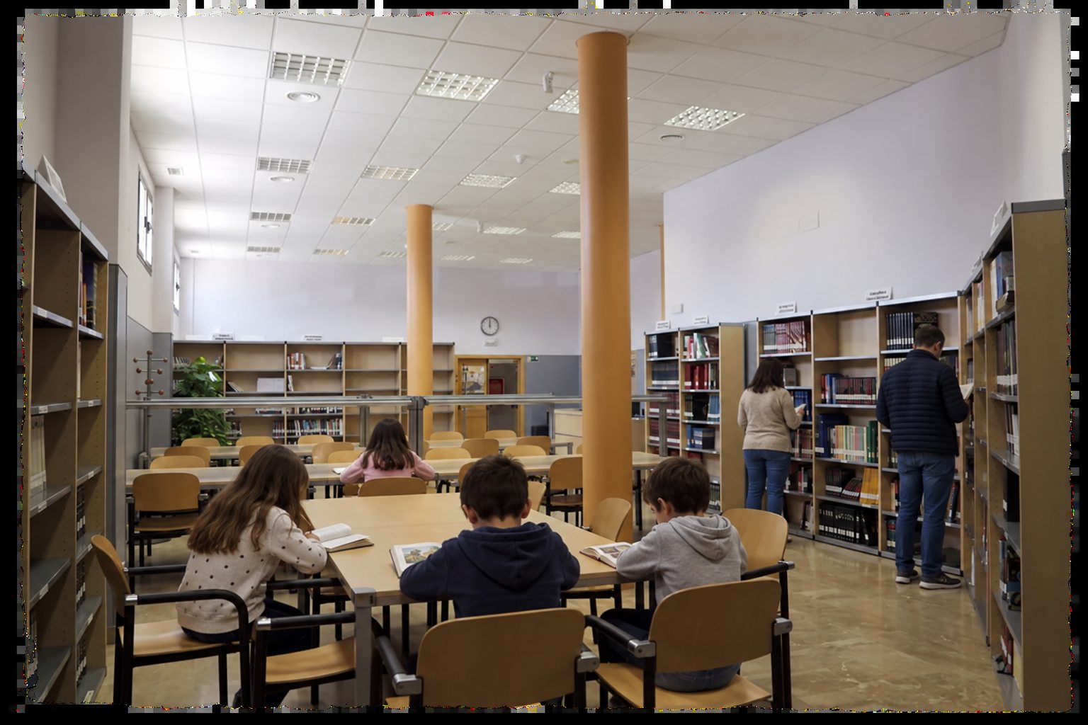 Niños leyendo y personas consultando las estanterías de la Biblioteca Municipal de Noblejas